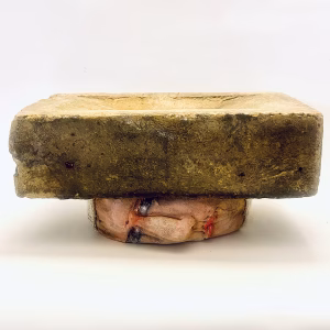 Small soft sculpture head crushed by a brick.