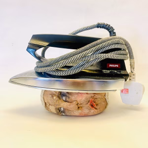 Small soft sculpture head crushed by a vintage iron.