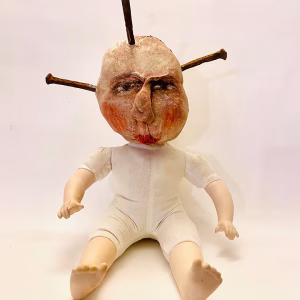 Hacked baby doll with head pierced by rusty nails.