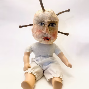 Hacked baby doll with head pierced by rusty nails.