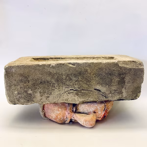 Soft sculpture head crushed by a brick
