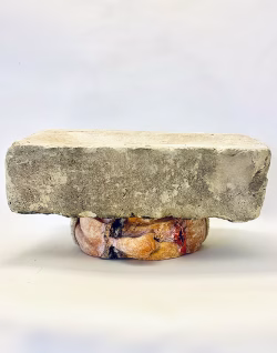 Soft sculpture head crushed by a brick