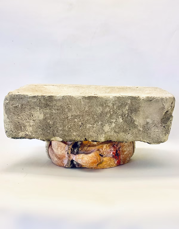 Soft sculpture head crushed by a brick