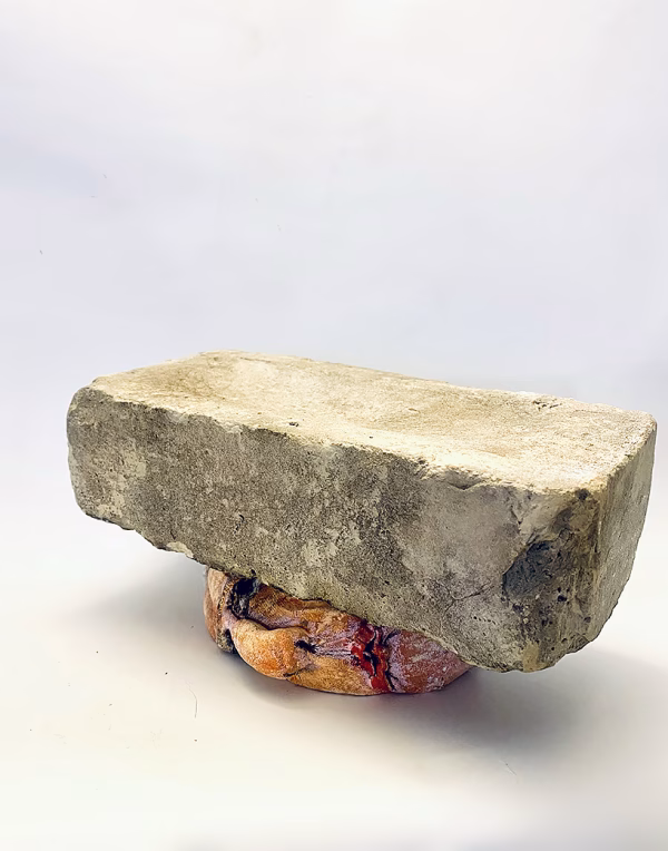 Soft sculpture head crushed by a brick