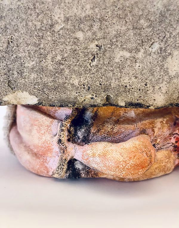 Soft sculpture head crushed by a brick