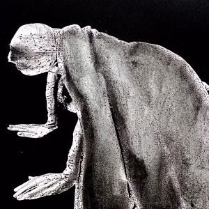 Laser cut woodprint of a woman crawling along the ground. She is bald, skeletal and covered in a removal blanket.