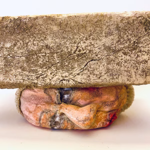 Small soft sculpture head crushed by a brick.