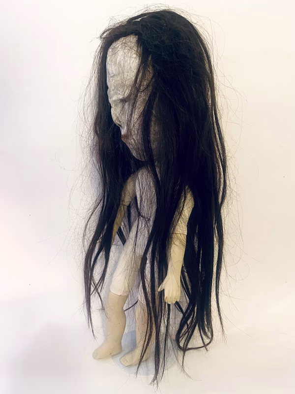 Uncanny girl doll with long dark brown hair.
