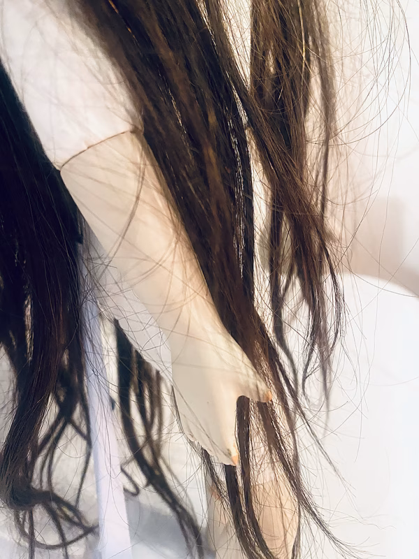 Uncanny girl doll with long dark brown hair. Detail view with hand, leg and hair.