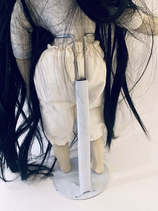 Uncanny girl doll with long dark brown hair. Back view with stand.