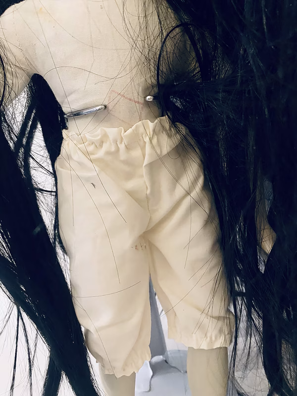 Uncanny girl doll with long dark brown hair. Hip view.