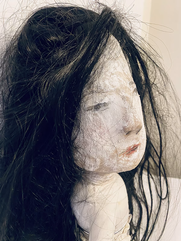 Uncanny girl doll with long dark brown hair. Face profile view.