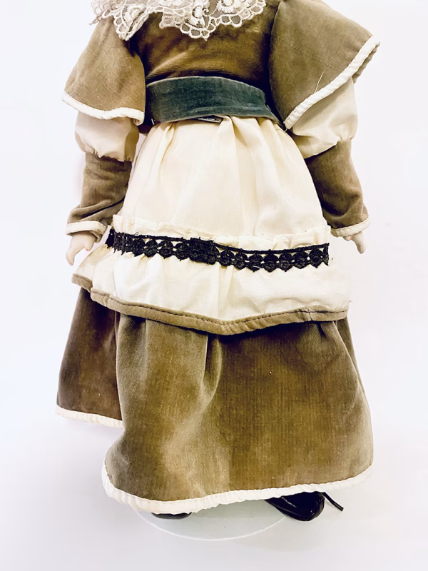 A doll wearing a sage green velvet and cream cotton dress.