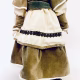 A doll wearing a sage green velvet and cream cotton dress.