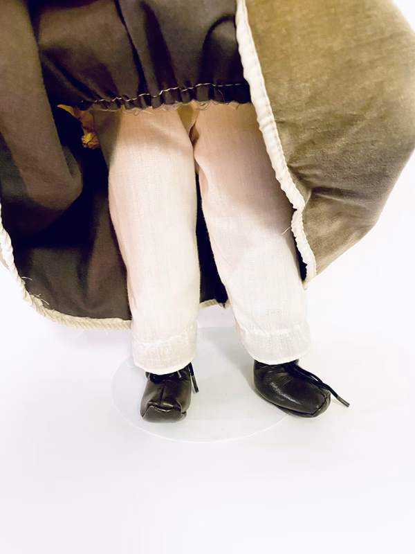 A doll wearing a sage green velvet and cream cotton dress. Uplifted skirt to show its legs.