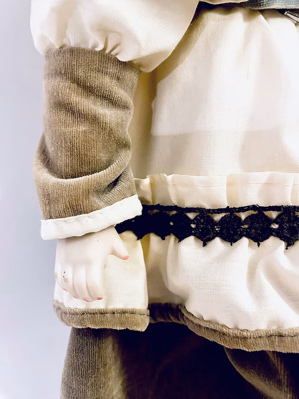 A doll wearing a sage green velvet and cream cotton dress. Close-up on right arm with hand an pink nails.