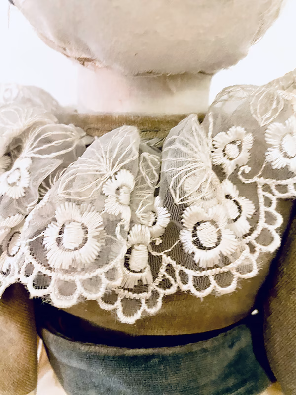 A doll wearing a sage green velvet and cream cotton dress. Close-up on lace collar.