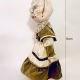 A doll wearing a sage green velvet and cream cotton dress. With a kilner jar clip over its head.