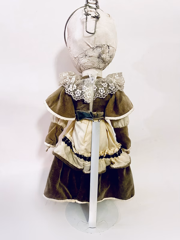 A doll wearing a sage green velvet and cream cotton dress. With a kilner jar clip over its head.