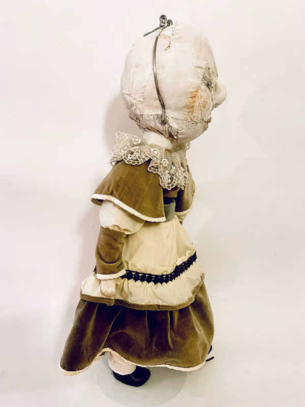 A doll wearing a sage green velvet and cream cotton dress. With a kilner jar clip over its head.