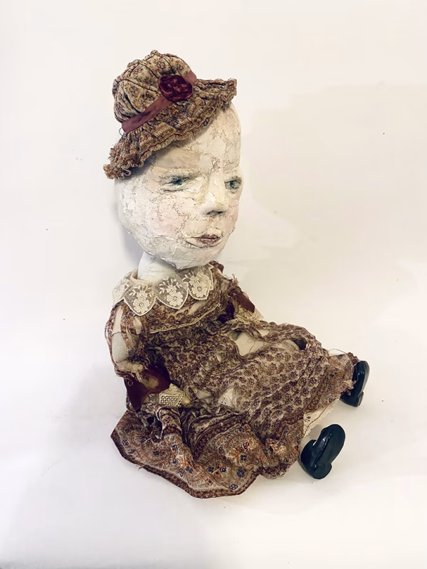 Hacked doll with decayed silk dress. The original ‘pretty’ head is replaced with an oversized, bald, uncanny head.