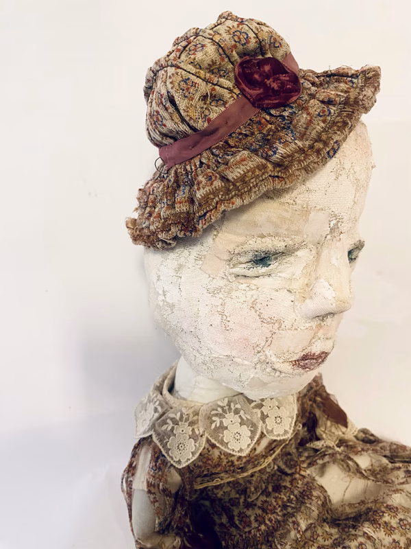 Hacked doll with decayed silk dress. The original ‘pretty’ head is replaced with an oversized, bald, uncanny head.