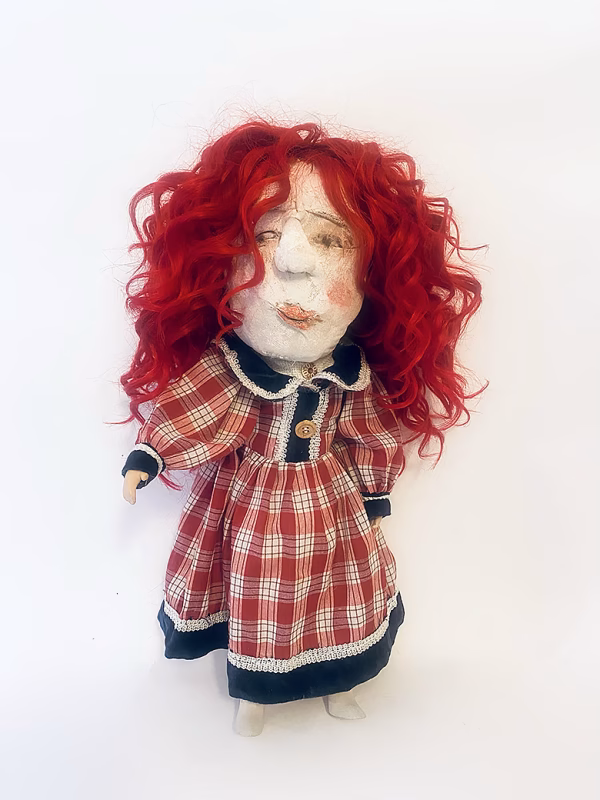 Uncanny girl doll with checkered dress and wavy red hair.