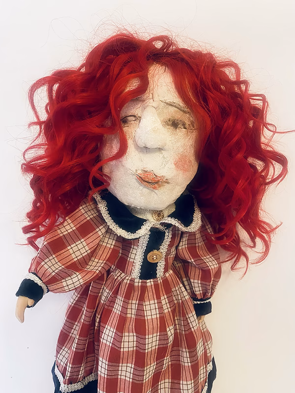 Uncanny girl doll with checkered dress and wavy red hair.