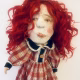Uncanny girl doll with checkered dress and wavy red hair.