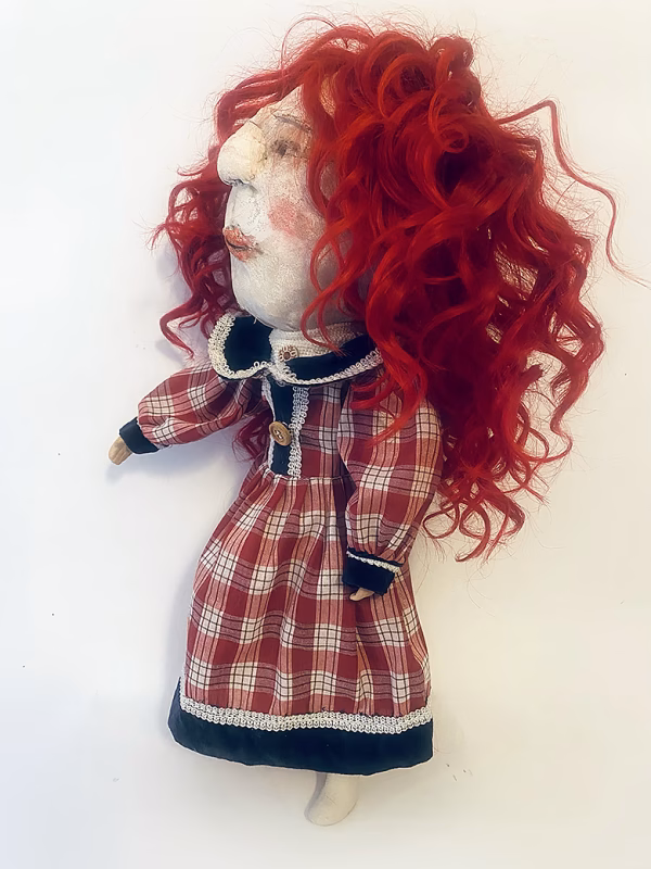 Uncanny girl doll with checkered dress and wavy red hair.