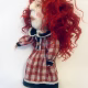 Uncanny girl doll with checkered dress and wavy red hair.