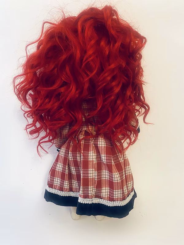 Uncanny girl doll with checkered dress and wavy red hair (back).