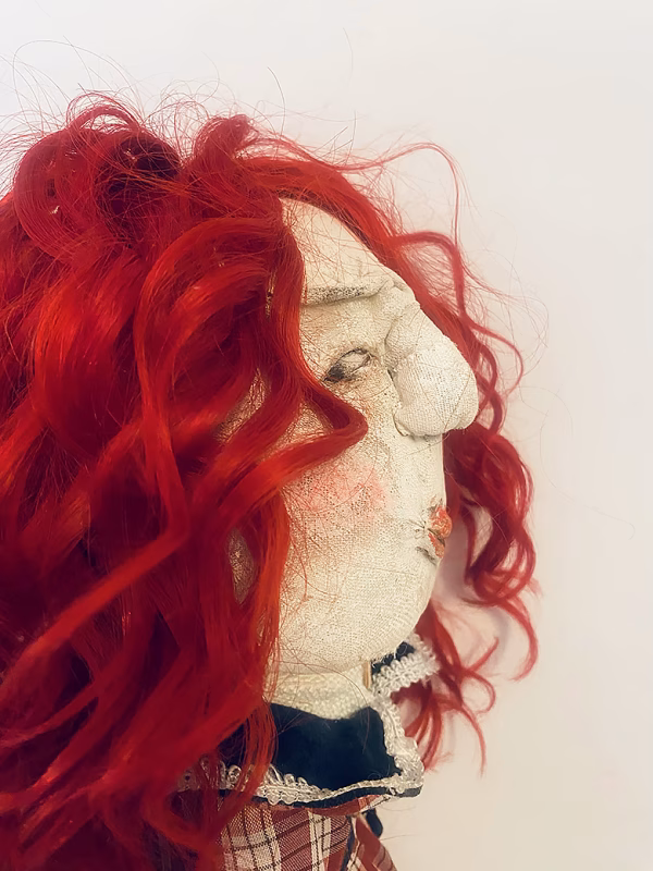 Uncanny girl doll with checkered dress and wavy red hair (face close-up).